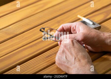 Hände, die Lesebrille mit einer angezündeten Zigarette vor einen Aschenbecher halten Stockfoto