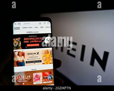 Person, die Smartphone mit Webseite des chinesischen E-Commerce-Unternehmens Shein auf dem Bildschirm vor dem Unternehmenslogo hält. Konzentrieren Sie sich auf die Mitte des Telefondisplays. Stockfoto