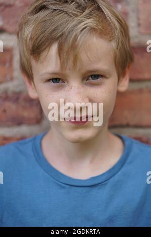 Porträt eines 11-jährigen hübschen blonden Jungen mit blauem T-Shirt an der Ziegelwand Stockfoto