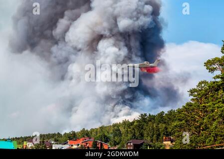 Großes amphibisches Feuerflugzeug tropft Wasser auf großes Waldfeuer in der Nähe des Dorfes Stockfoto