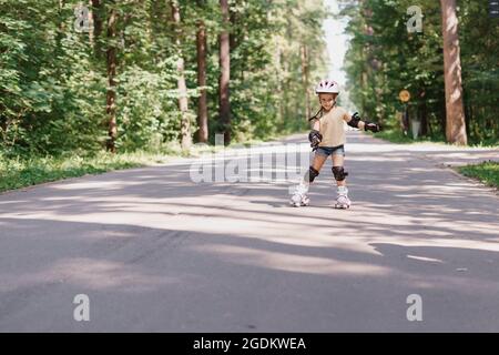 Kleines Mädchen ist Rollerblading im Park. Baby in schützender Sportkleidung Stockfoto