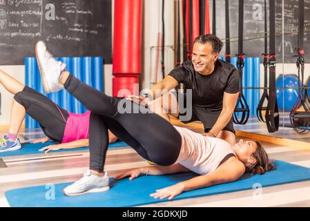 Frauen, die mit einem Bein nach oben mit Hilfe eines Trainers im Fitnessstudio trainieren Stockfoto