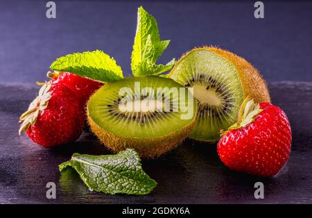 Ein Stillleben-Foto von frischen reifen Früchten, verziert mit Minzblättern auf dem dunklen Hintergrund und Reflexionen auf einem nassen Tisch. Natürliche Produkte, Ernte. Stockfoto
