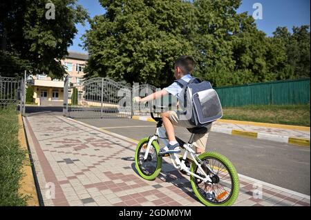 Rückansicht eines Kindes auf einem Fahrrad am frühen Morgen. Junge auf dem Fahrrad in der Stadt. Zurück zur Schule Stockfoto