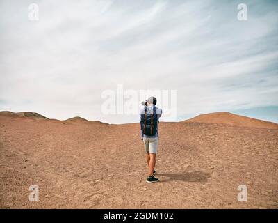 asiatischer, männlicher Backpacker-Landschaftsfotograf, der ein Foto auf einem Hügel macht, Rückansicht Stockfoto