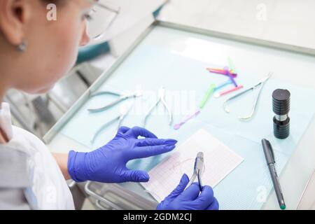 Zugeschnittenes Bild eines professionellen Kieferorthopäden, der Instrumente zur Anwendung von Zahnspangen auf die Zähne des Patienten vorbereitet Stockfoto