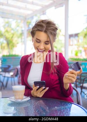 Fröhliche lächelnde Frau mit Smartphone und Kreditkarte während der Kaffeepause. Online-Shopping und Online-Handel Konzept. Stockfoto