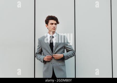 Seriöse junge kaukasische Kerl professionell gekleidet posiert vor einer grauen Wand Stockfoto