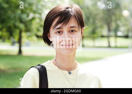 Nahaufnahme einer jungen Frau mit kurzen Haaren, die an sonnigen Tagen im Freien auf die Kamera schaut Stockfoto