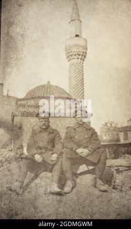 Ein Porträt zweier britischer Soldaten aus dem Ersten Weltkrieg in Mänteln, die vor einer Moschee mit einem burmalı-Minarett (verdreht/spiralförmig) sitzen. Es wird angenommen, dass die Nahost-Kampagnen gegen das Osmanische Reich gelangten. Stockfoto