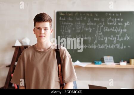 Porträt eines Schuljungen mit Rucksack, der die Kamera anschaut, während er in einem leeren Klassenzimmer steht Stockfoto