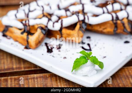 Waffeln In Nahaufnahme. Belgische Waffeln mit Schlagsahne und Schokoladensirup, serviert und verzehrt. Selektiver Fokus Stockfoto