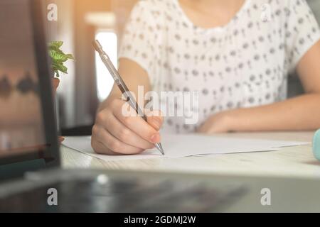 Hand einer Frau mit Bleistift und Schreiben auf Papier Dokument im Büro. Holztisch mit Laptop und Arbeitsbereich Stockfoto