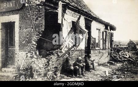 Eine historische Ansicht von drei französischen Soldaten, die sich während der Somme-Offensive 1916 während des Ersten Weltkriegs gegen das vom Kampf zerstörte Restaurant Lanne in Herbecourt ausruhen. Stockfoto