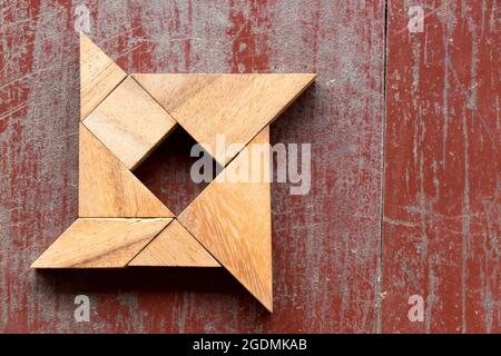 Tangram Puzzle in Shuriken-Form auf rotem alten Holz Hintergrund Stockfoto