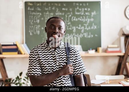 Porträt eines afrikanischen Studenten mit Rucksack, der die Kamera anlächelt, während er im Klassenzimmer steht Stockfoto