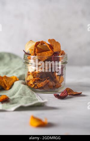 Gemüsechips aus Kartoffeln, Rüben und Karotten in einem Glas und mit einer Serviette auf einen betonierten Hintergrund gelegt Stockfoto