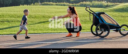 Aktive Mutter mit Kind mit Jogging-Kinderwagen zum Laufen im Park. Glückliche Mutter und ihr Sohn haben Spaß im Freien Stockfoto