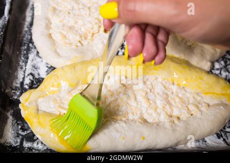 Weibliche Hände putzen süße Backwaren mit Eigelb, mit Silikonbürste. Stockfoto