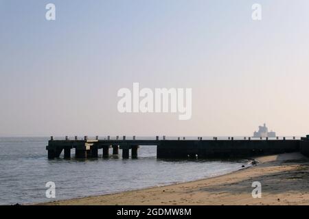 Fischerpier Hafen für Fischerboote an einem Sandstrand mit einem Leuchtturm im Hintergrund. Aufgenommen am Morgen bei hellem Tageslicht in einer Küstenstadt. Stockfoto