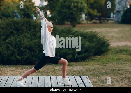 Porträt einer jungen, lächelnden, tausendjährigen europäischen Kurzhaarigen, die im Park Yoga macht. Schöne glücklich blonde Mädchen im Freien. Stockfoto