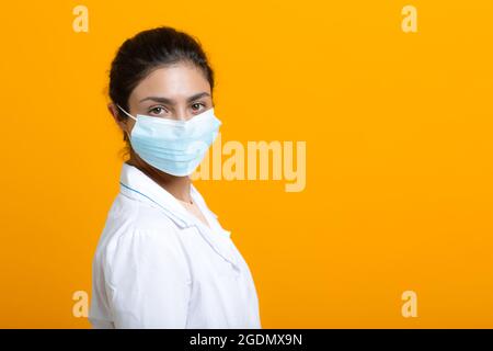 Porträt der indischen Ärztin in weißem medizinischen Kleid und Gesichtsmaske isolieren auf gelbem Hintergrund. Stockfoto
