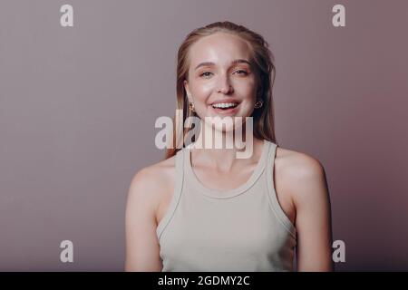 Porträt einer jungen lächelnden europäischen Frau. Schönes glückliches blondes Mädchen trägt T-Shirt und schaut in die Kamera. Studio-Aufnahmen auf rosa Hintergrund isoliert. Stockfoto