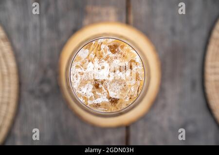 Eiskaffee am Morgen auf einem alten Holztisch, der die Textur von Eis auf Glas zeigt. Stockfoto