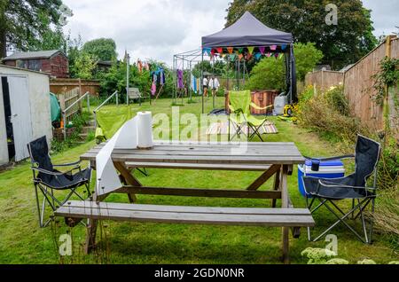 Ein Garten mit einem Holztisch und einer Bank, die im Vorgarten aufgestellt ist, und einem gemieteten Whirlpool unter einem Pavillon dahinter. Stockfoto