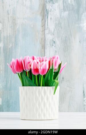 Rosa Tulpen in weißer Keramikvase, blauer Holzhintergrund. Stockfoto