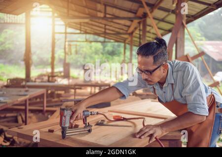 Nahaufnahme eines Mannes Zimmermann mit einem Nagel gun.Carpenter mit Luft Nagelpistole tun Holzmöbel Arbeit, Vintage-Stil Stockfoto