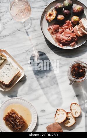 Rosenwein im Glas, Honigwabe, Käse, hausgemachte Feigenmarmelade im Glas, Brotscheiben und Teller mit frischen Feigen und Prosciutto-Fleisch über grauem Marmor-Backgro Stockfoto