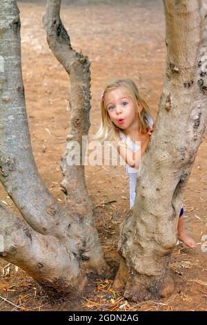 Ein 2-jähriges Mädchen spielt sich hinter einem Baum verstecken und suchen Stockfoto