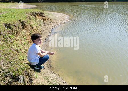 8-jähriges brasilianisches Kind, geduckt am See, angeln an einem sonnigen Morgen. Stockfoto