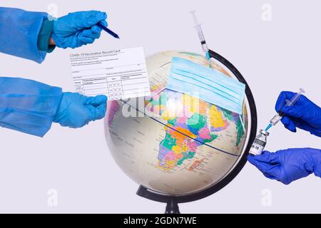 Nahaufnahme des Globus und der Hände der beiden Ärzte in medizinischen Handschuhen mit Impfzertifikat und Impfdosis mit Spritze. Stockfoto