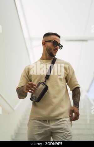 Junger Mann mit Sonnenbrille in weißen Kleidern, der im Abuilding steht Stockfoto