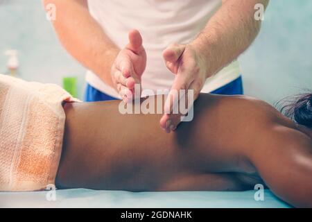 Massage aus der Nähe. Afroamerikanische Frau bekommt eine Massage. Eine Physiotherapeutin macht eine Rückenmassage für eine schwarze Frau. Stockfoto