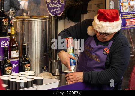 Der Weihnachtsmarkt-Ladenbesitzer trägt einen Hut von der Santa Claus-Creme auf einer kleinen Tasse heißer Schokolade, Harrogate North Yorkshire, England, Großbritannien. Stockfoto