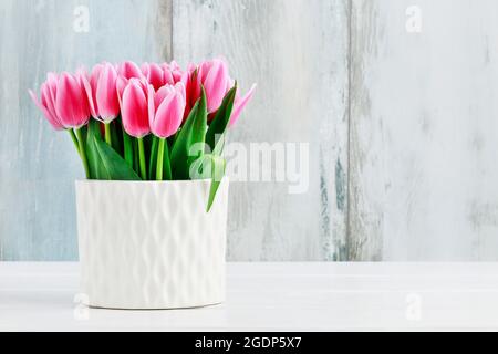 Rosa Tulpen in weißer Keramikvase, blauer Holzhintergrund. Stockfoto