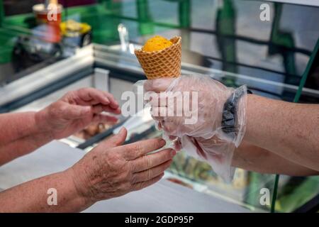 Der Verkäufer gibt einem Kunden zur Sommerzeit einen Ball mit einem leckeren Fruchteis in einem Laden Stockfoto