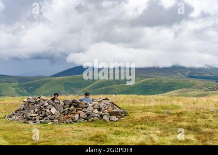 Zwei Wanderer nehmen in einem Steinring in der Nähe des Gipfels von Windy Gyle an der Grenze zu England Schottland in den Cheviot Hills, Northumberland, Schutz. Stockfoto