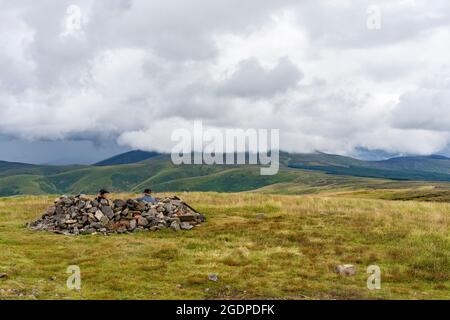 Zwei Wanderer nehmen in einem Steinring in der Nähe des Gipfels von Windy Gyle an der Grenze zu England Schottland in den Cheviot Hills, Northumberland, Schutz. Stockfoto