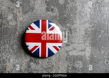 Die Flagge Großbritanniens, allgemein bekannt als Union Jack, gedruckt auf einem Knopfabzeichen, liegt auf grauem Steingrund. Stockfoto