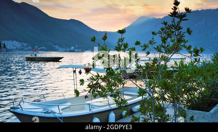 Wunderschöne Abenddämmerung beschauliches Wasser und untergehende Sonne hinter fernen Bergen, Boote und Laub im Vordergrund. Stockfoto