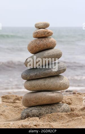 Ein ausgewogener Turm aus glatten Strandfelsen auf dem Sand in der Nähe des Ozeans Stockfoto