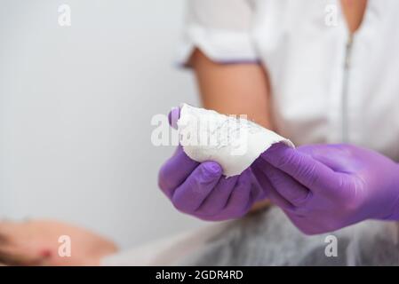 Hand mit lila Handschuhen halten gebrauchte Wachsstreifen mit entfernten Haaren. Enthaarungshaut im Spa-Salon Stockfoto