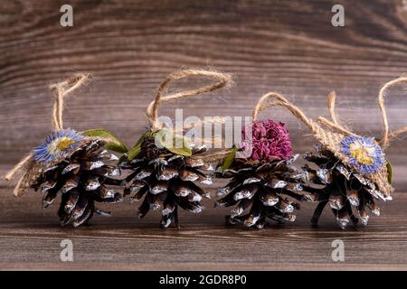 Handgemachtes Weihnachtsbaumspielzeug aus Kiefernzapfen, verziert mit natürlichen Materialien, vor dem Hintergrund eines geschnittenen Baumes. Dekorationen mit Hanf-Suspension Stockfoto