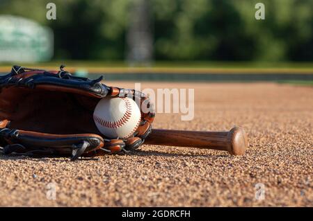 Baseballspiel in einem Fäustling mit einem braunen Schläger mit niedrigem Winkel und selektivem Fokus auf einem Baseballfeld Stockfoto