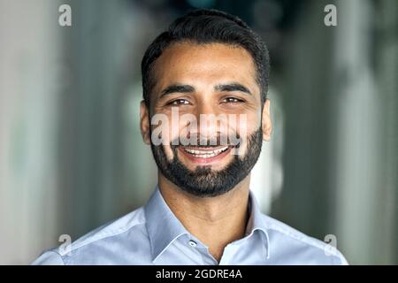 Lächelnder, selbstbewusster indischer Geschäftsmann, der die Kamera im Büro ansieht. Stockfoto