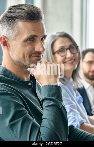Lächelnder, reifer Geschäftsmann, der mit dem Führungsteam am Schreibtisch sitzt. Stockfoto